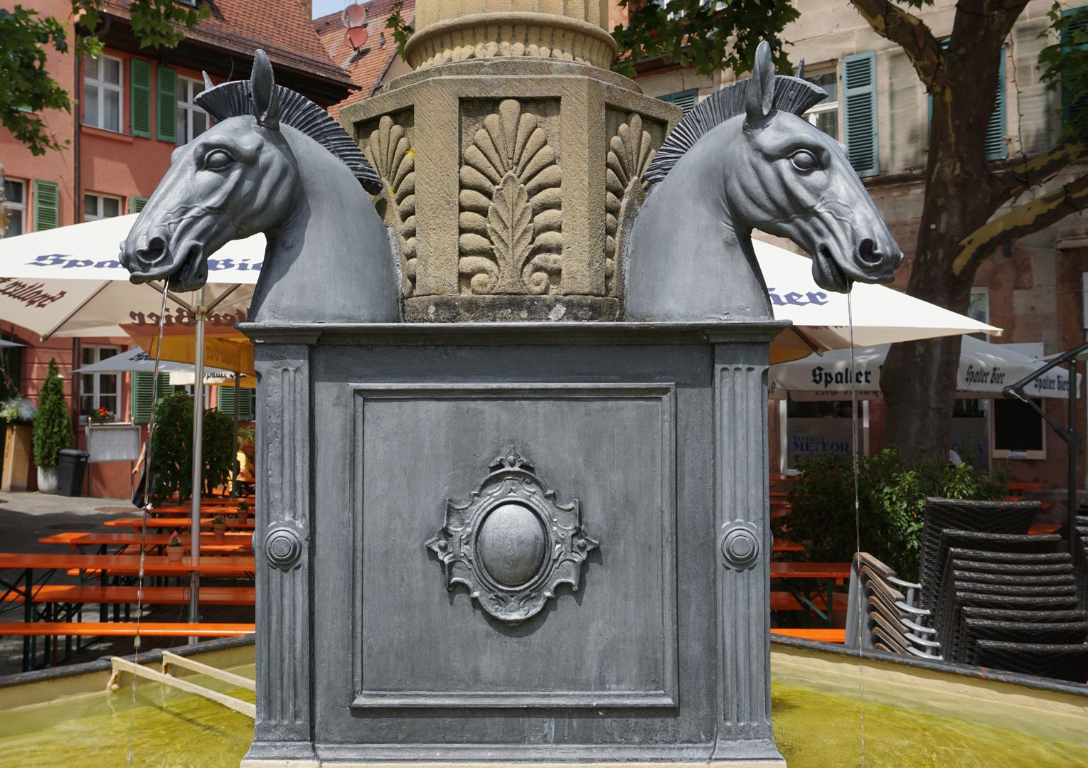 Pferdebrunnen Sockel mit 4 über Eck gestellten Pferdeköpfen, welche auf die Nutzung als Pferdetränke verweisen.